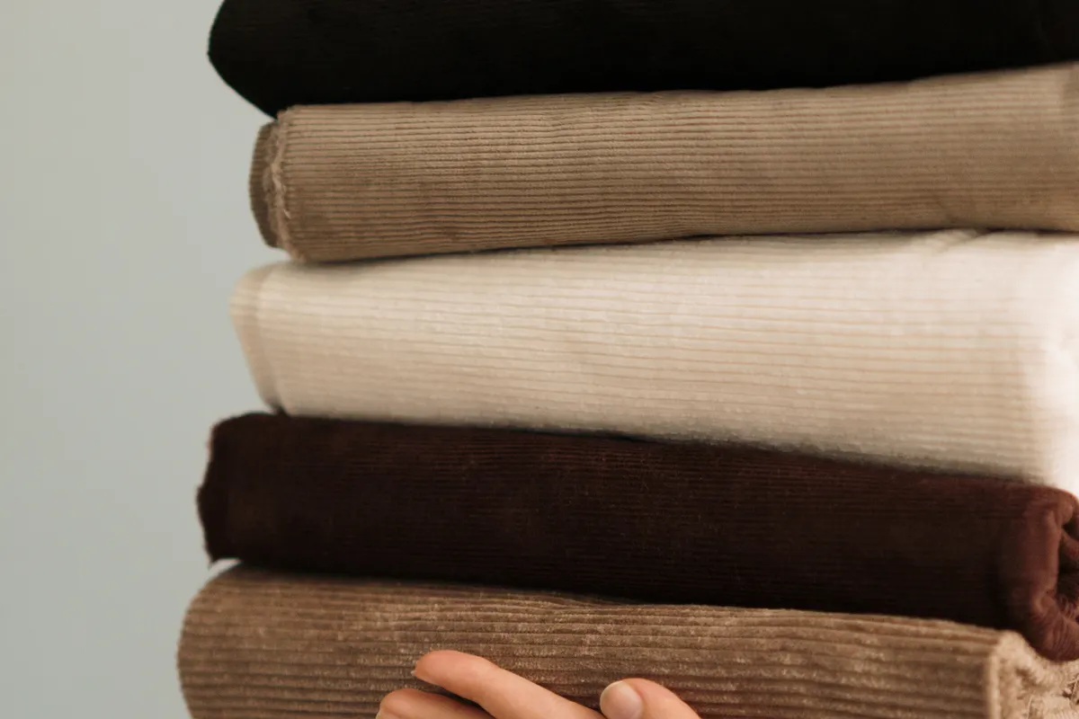 A hand holding a stack of folded clothes in black, taupe, cream, dark brown and tan