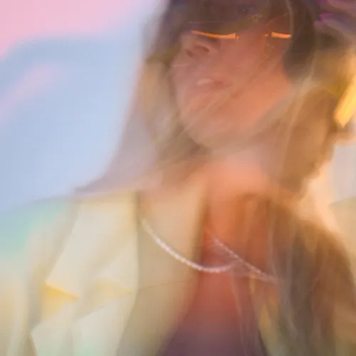 A motion-blurred portrait of a woman in sunglasses against a pastel pink and blue background