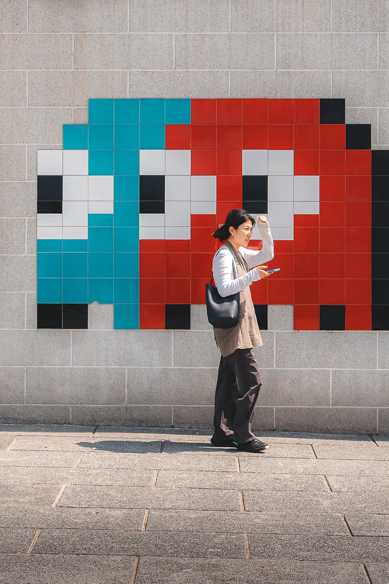 A woman checking her phone as she walks past a wall of giant pixel-art Space Invaders in blue and red