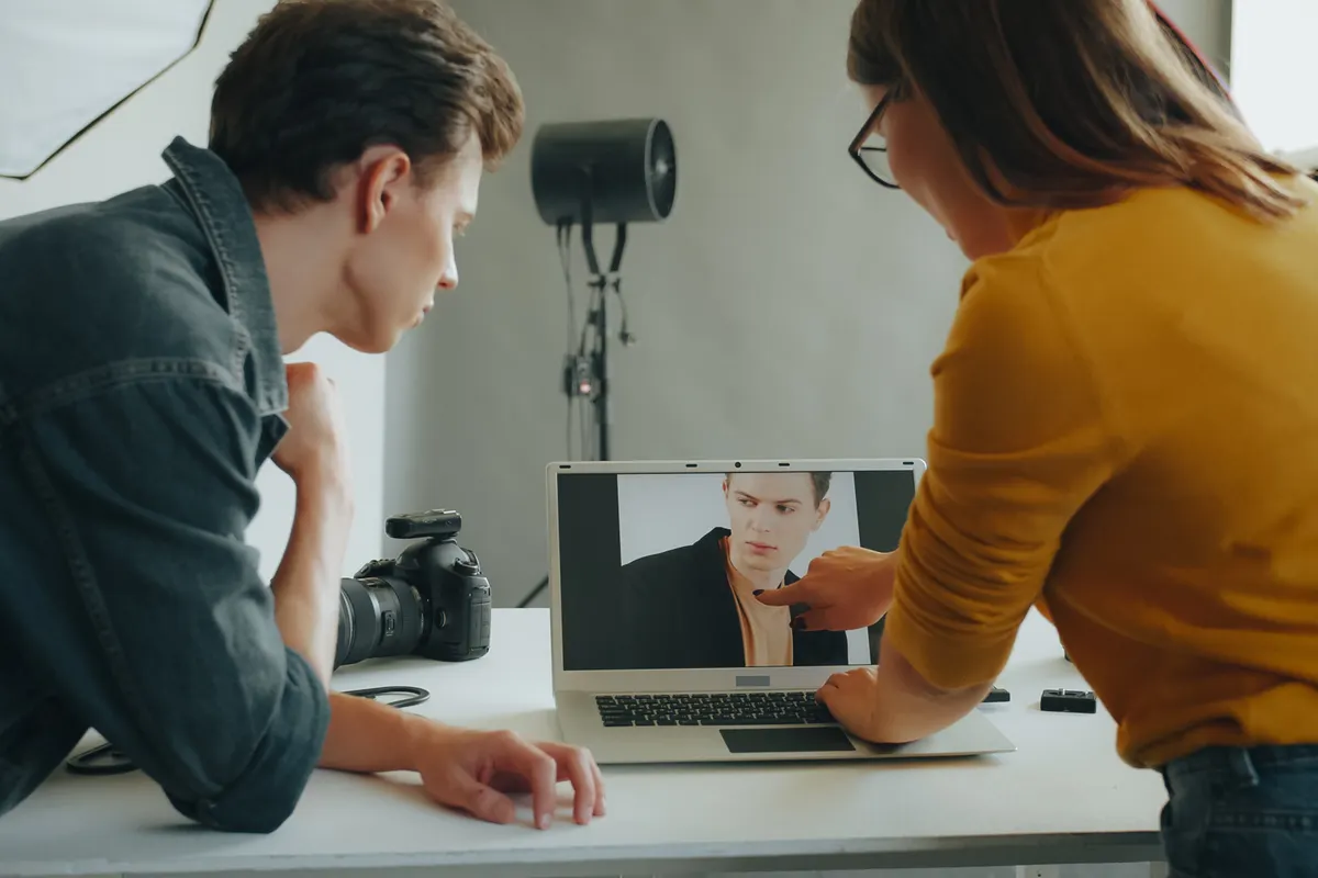 Two photographers in a studio leaning over a laptop to check a portrait at full size