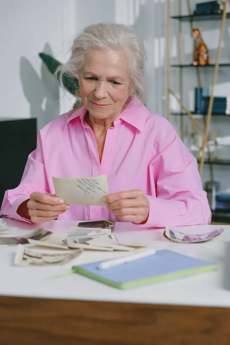 A woman in a pink shirt holding an old photograph at a table covered in vintage prints