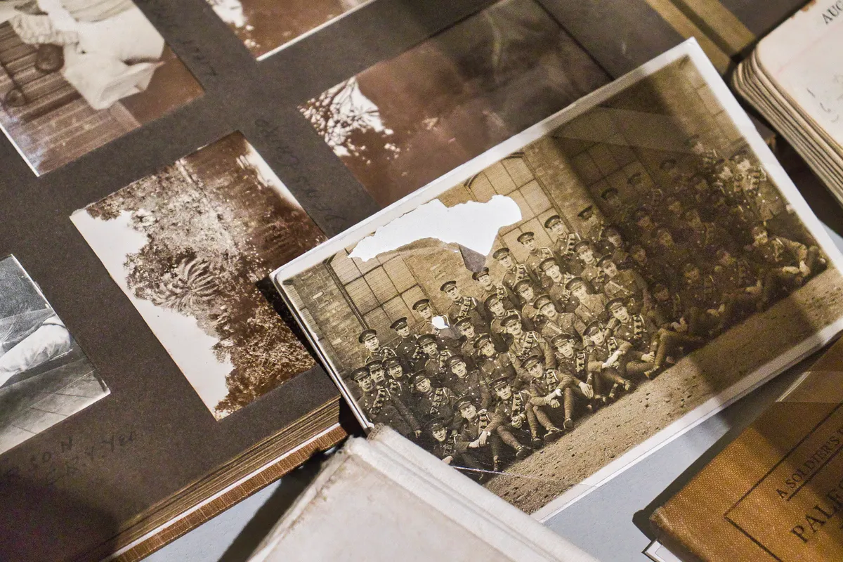 A sepia group photograph of uniformed men with a piece torn from its top corner, lying on an old album