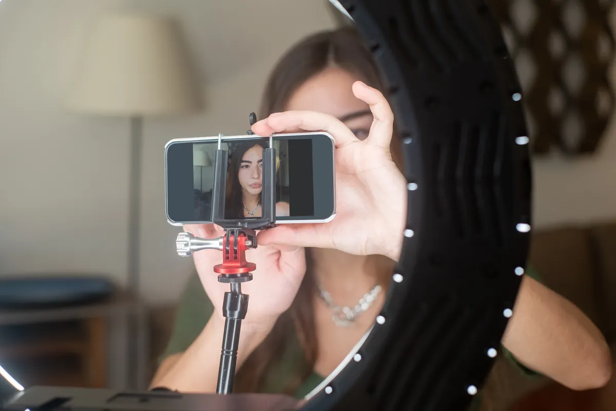 A phone mounted on a small tripod inside a ring light, with a woman's face showing on its screen