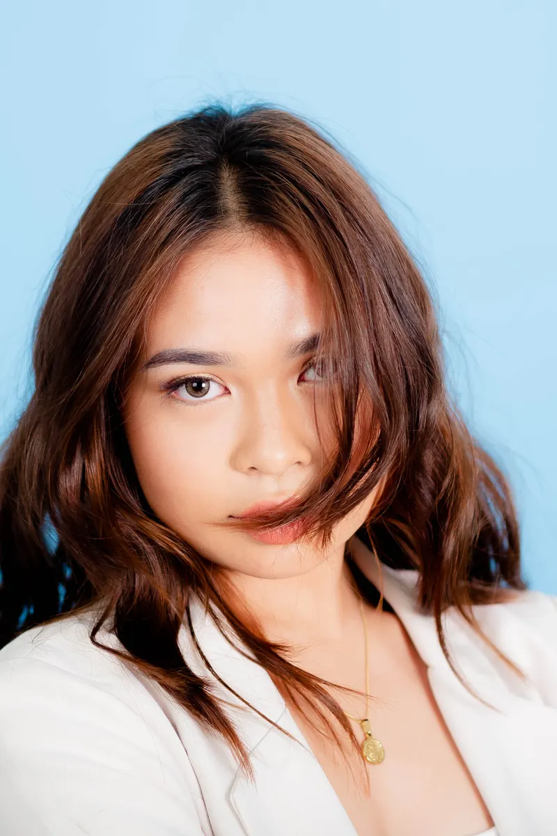 Woman with warm chestnut brown hair against a pale blue studio background