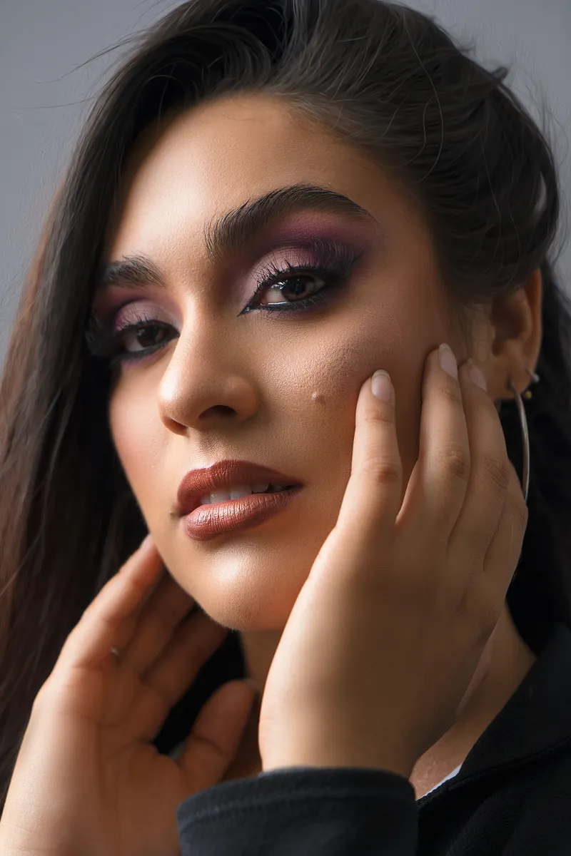 A close-up portrait of a woman wearing a purple smoky eye and a warm brown lip