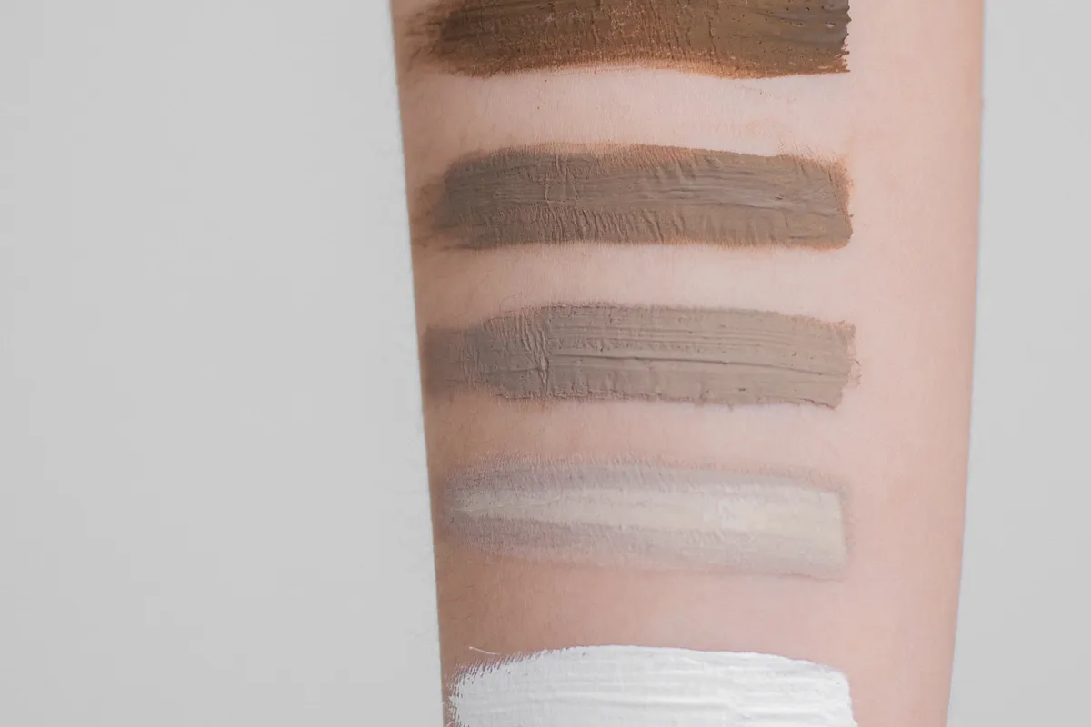 Five shades of foundation swatched in stripes down a forearm, from deep brown to near white