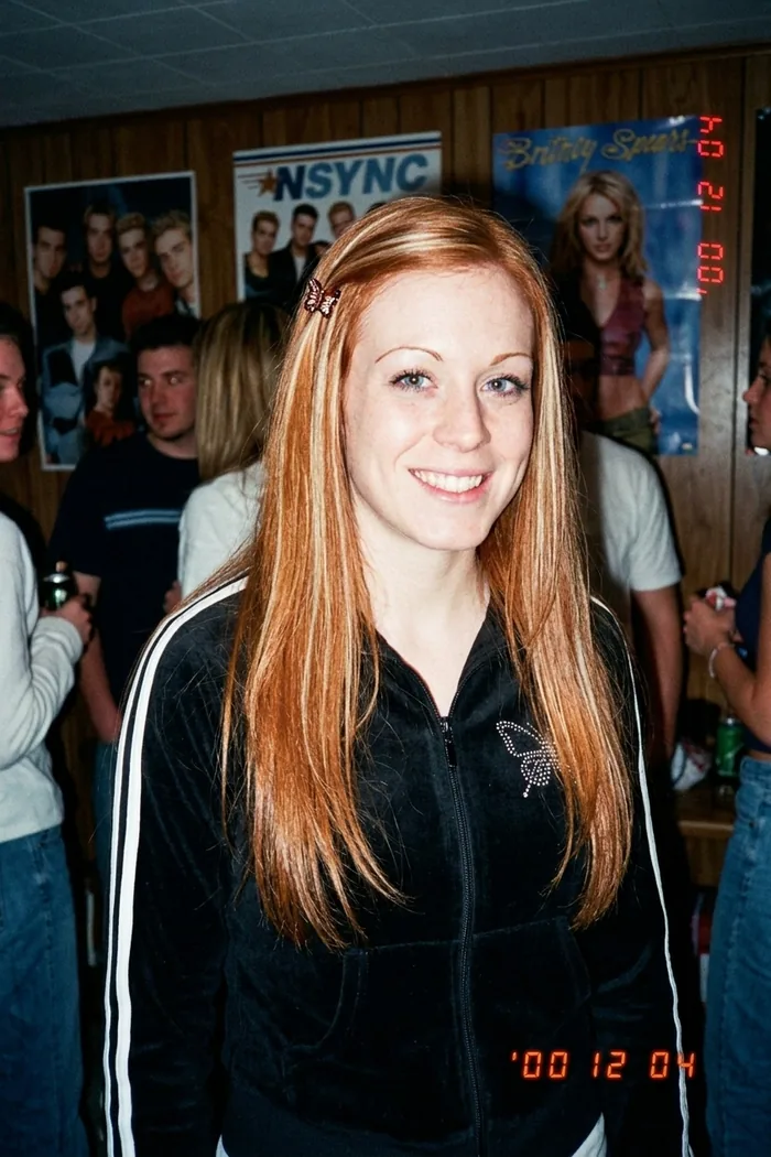 The same woman at a Y2K house party in a velour tracksuit, shot on a digicam
